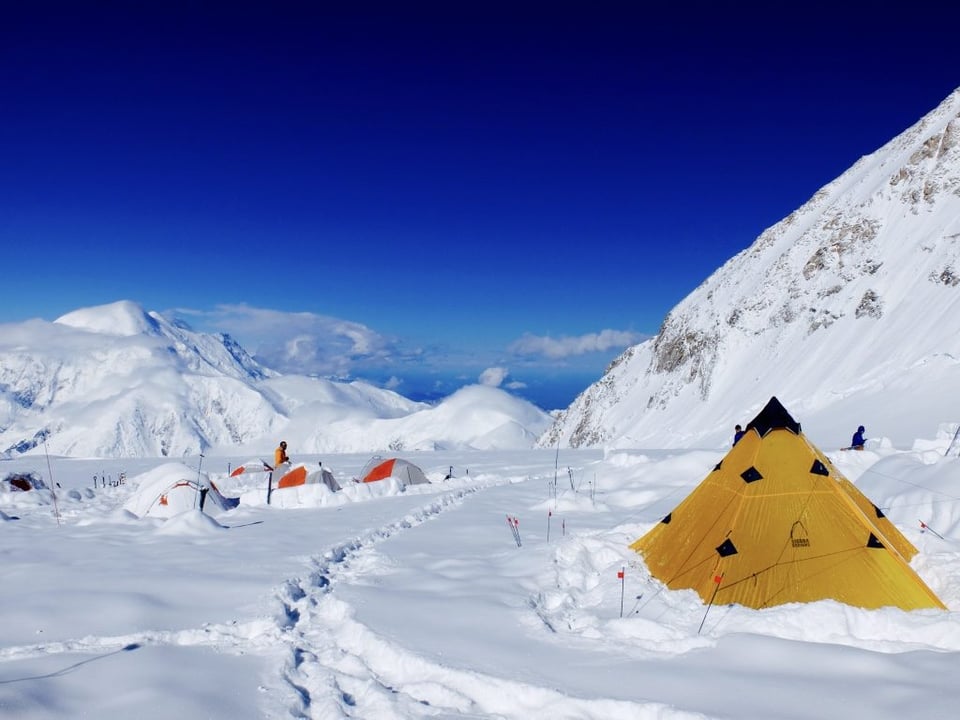 Tents buried in snow around Denali on a sunny day.